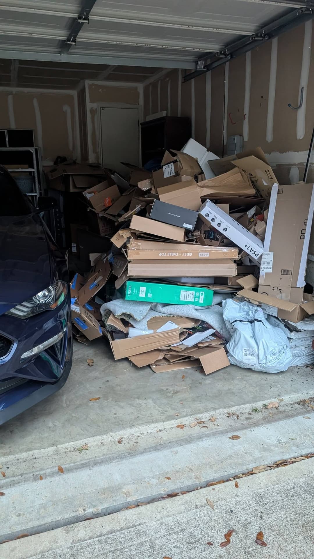 Overflowing garage filled with cardboard boxes and clutter next to a parked car.