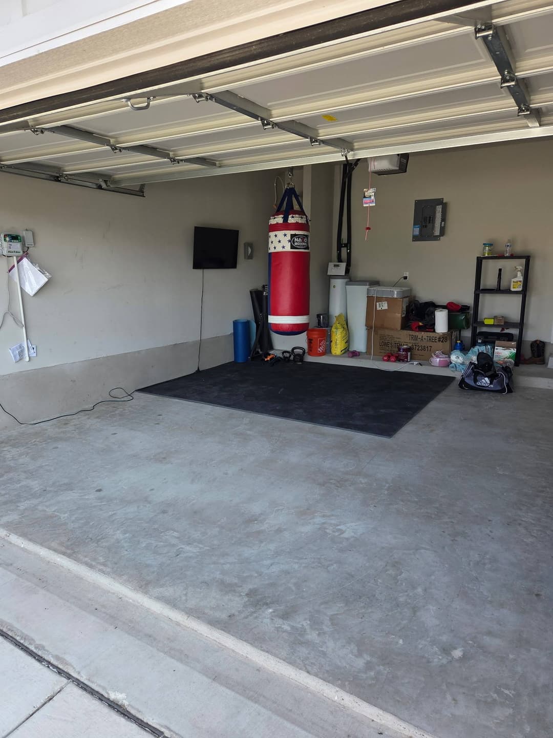 Empty garage interior featuring a red and white punching bag, exercise equipment, and storage boxes.