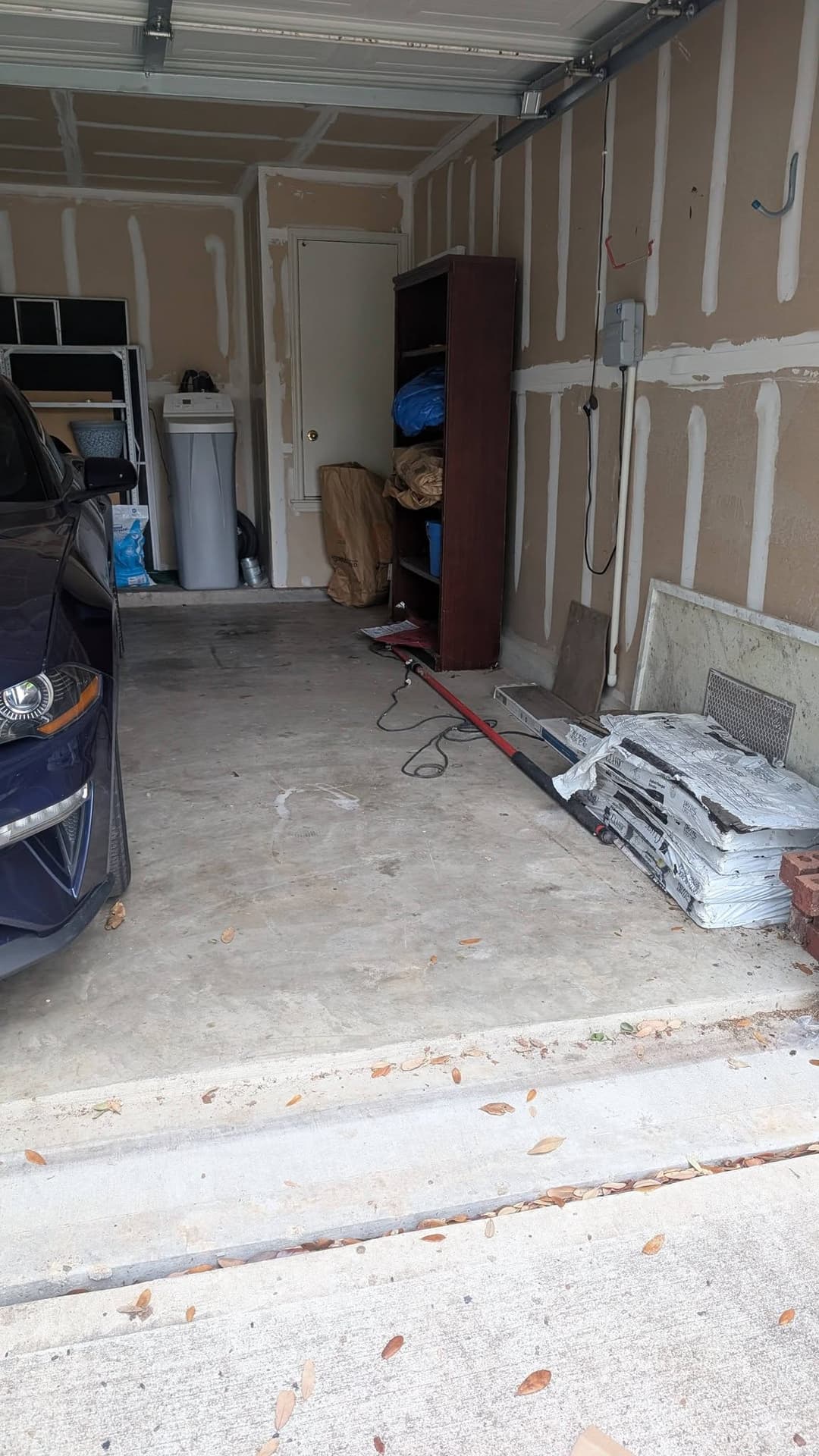 Garage interior with a parked car, storage shelves, and construction materials.