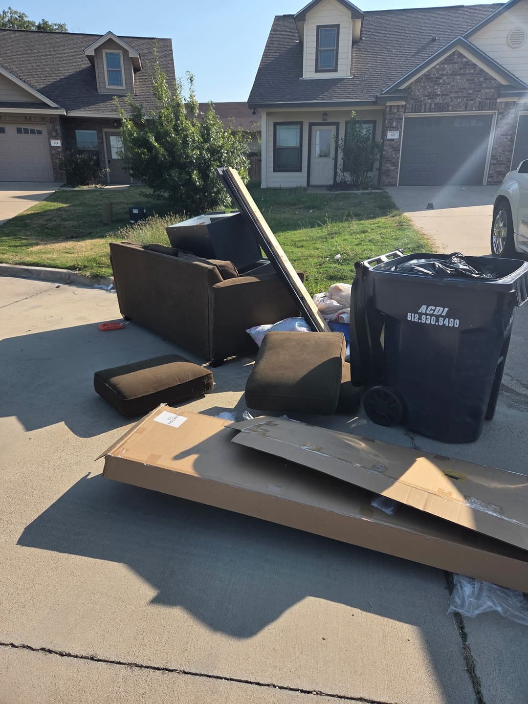 Discarded furniture and cardboard boxes outside a residential home on a sunny day.