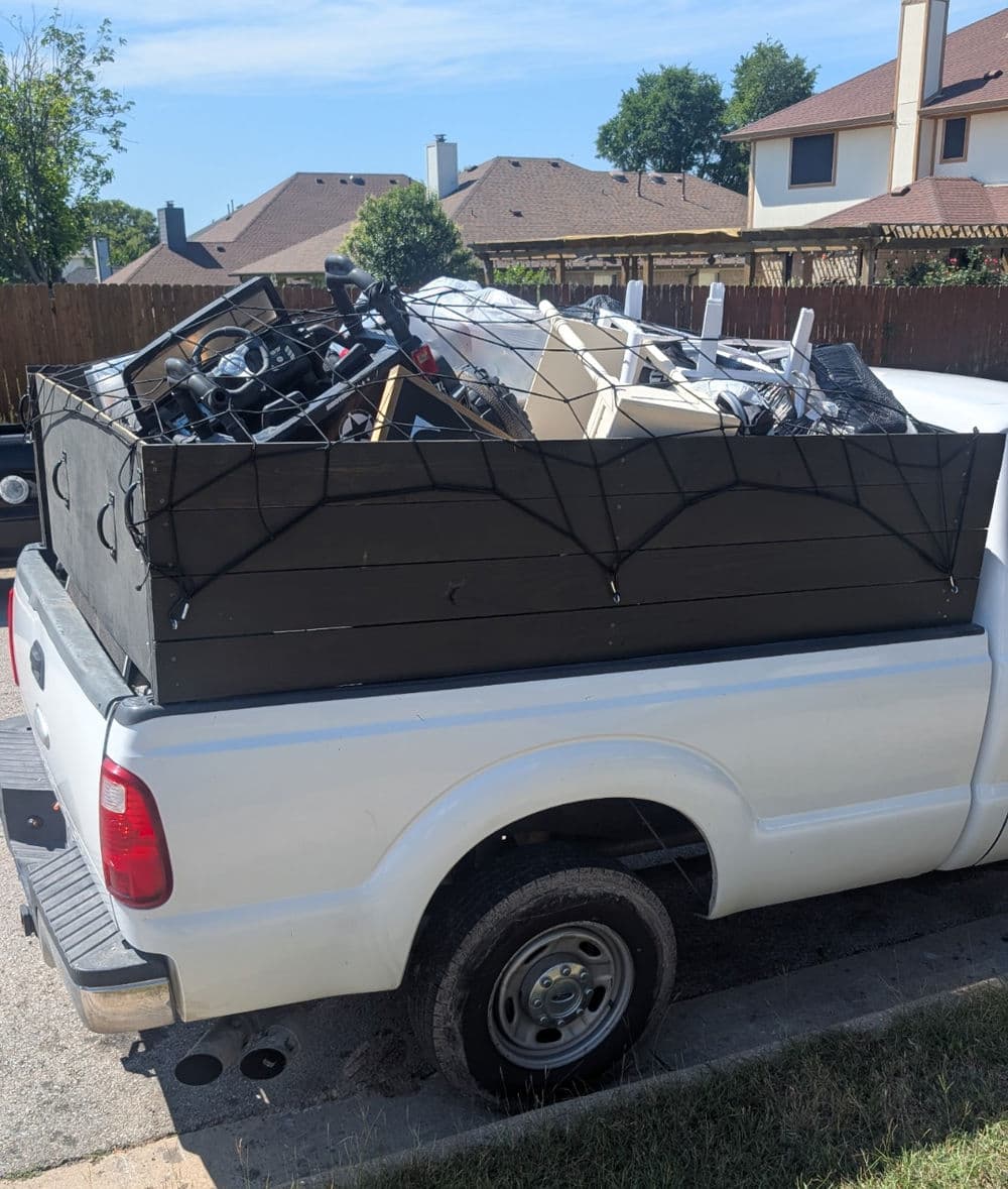 Pickup truck filled with various discarded items secured with a net in a residential area.