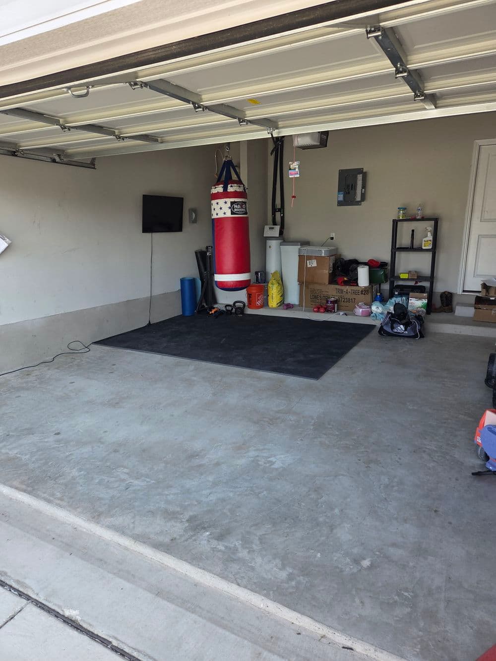 Empty garage with a red punching bag, exercise mat, TV, and various storage items.